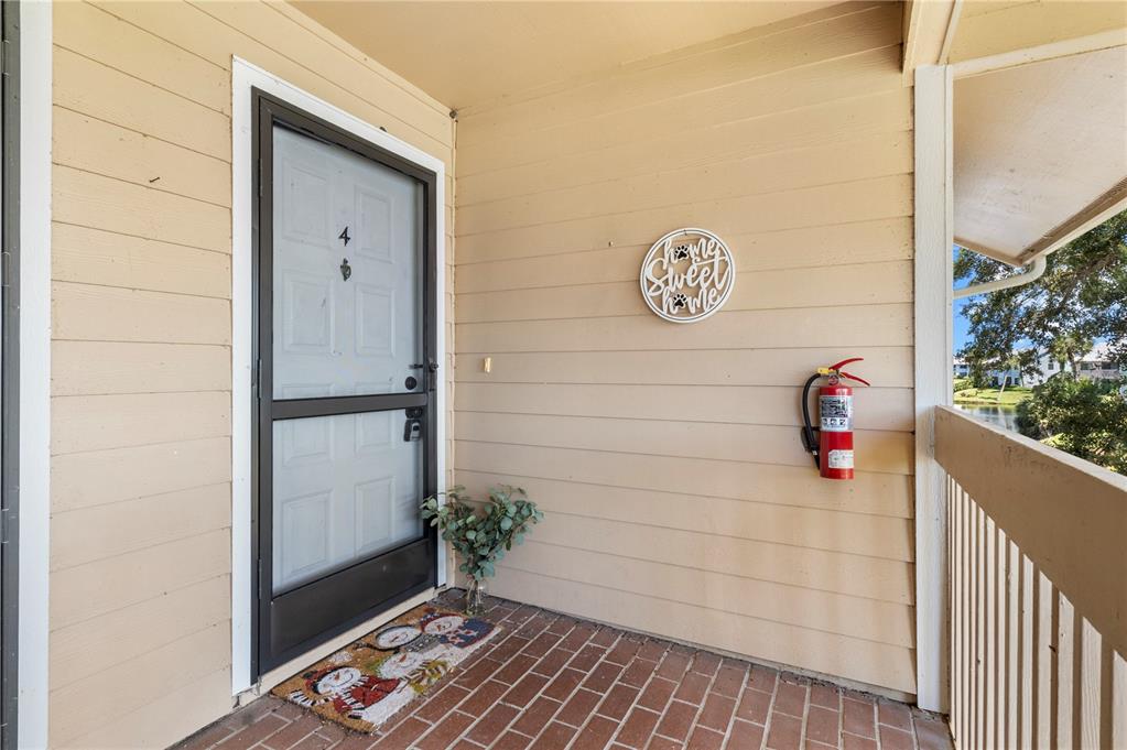 A brick-floored apartment entryway features a screen door, a fire extinguisher, and a wall sign — 5685 MARINA DRIVE UNIT 4, SEBASTIAN, FL