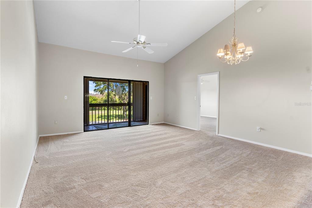 A carpeted living room features a vaulted ceiling, a ceiling fan, and sliding glass doors — 5685 MARINA DRIVE UNIT 4, SEBASTIAN, FL
