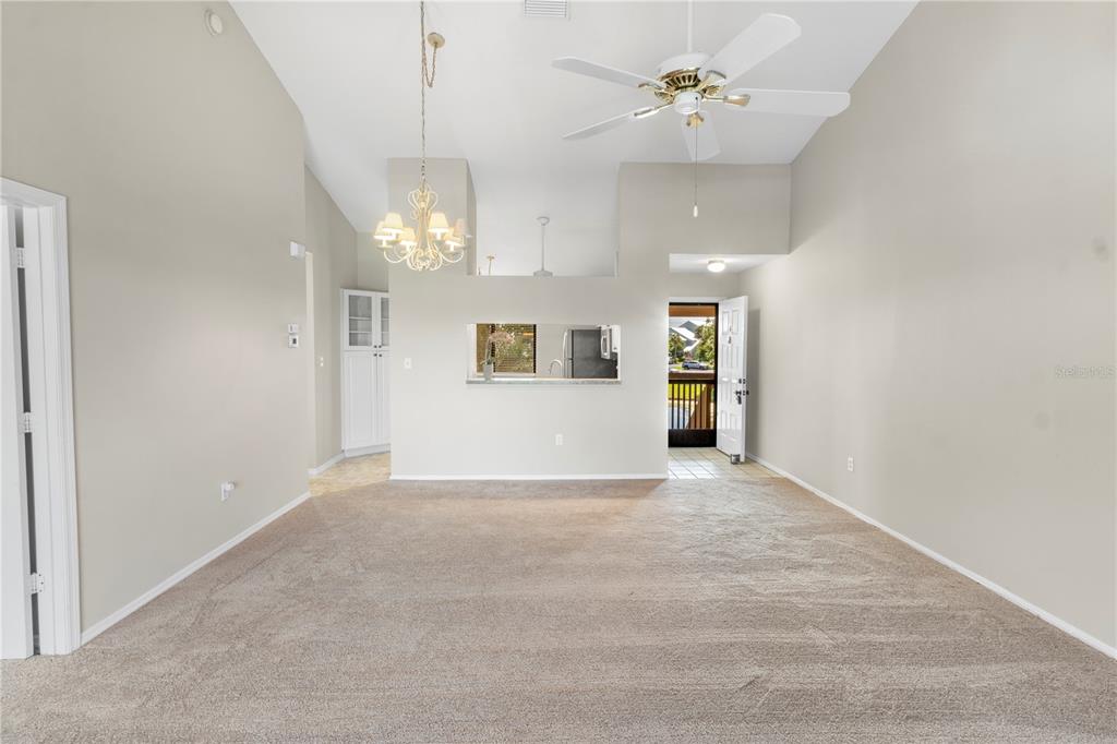 A living room with beige carpet, a vaulted ceiling, a ceiling fan, and a pass-through window — 5685 MARINA DRIVE UNIT 4, SEBASTIAN, FL