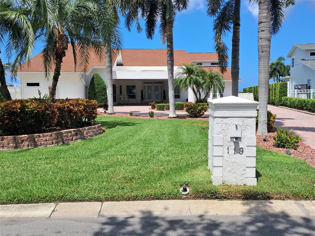 A white house with a brown roof sits behind a lawn and a stone mailbox — 119 CARLYLE CIRCLE, PALM HARBOR, FL