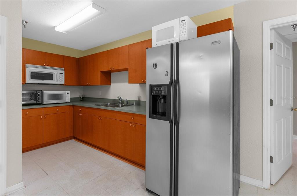 A kitchen features wood cabinets, a stainless steel refrigerator, and a microwave on the counter — 7044 COMMERCIAL WAY, WEEKI WACHEE, FL
