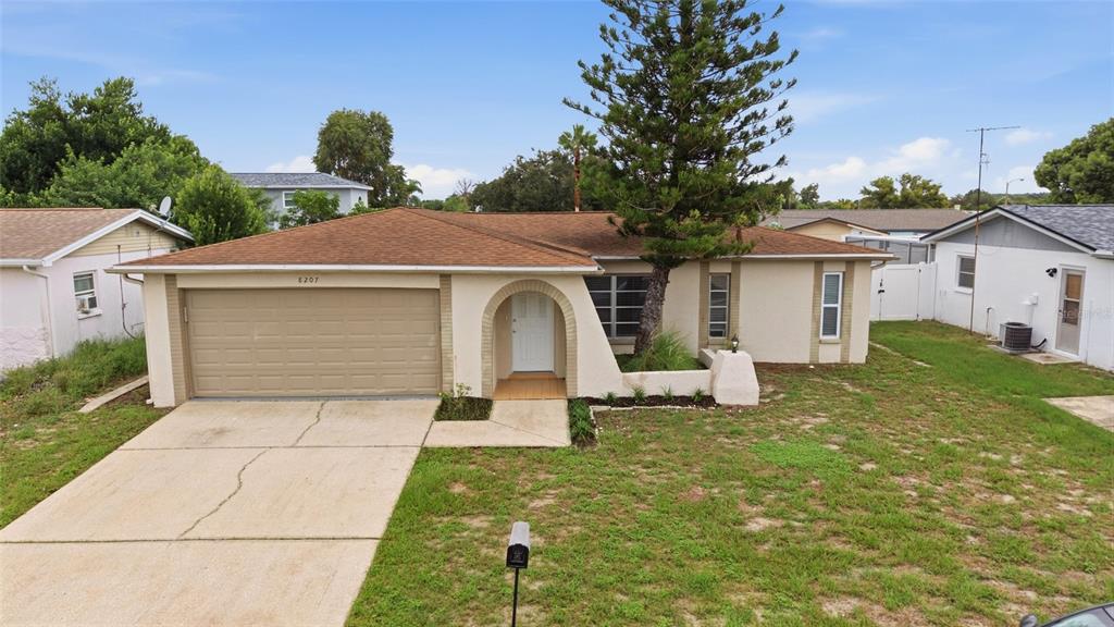 A single-story house with a tan stucco exterior, a brown roof, and an arched entryway — 8207 DEDHAM DRIVE, PORT RICHEY, FL