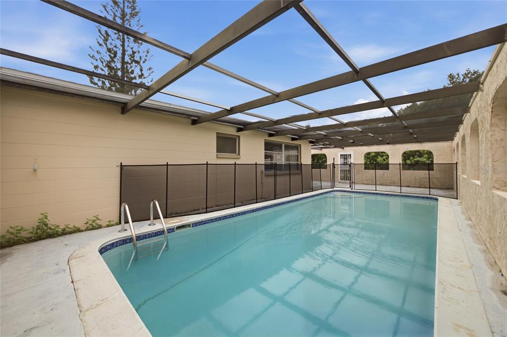 A rectangular swimming pool is enclosed by a screened lanai with a black safety fence — 8207 DEDHAM DRIVE, PORT RICHEY, FL