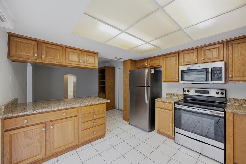A kitchen with oak cabinets, granite countertops, stainless steel appliances, and a grid ceiling light — 8207 DEDHAM DRIVE, PORT RICHEY, FL