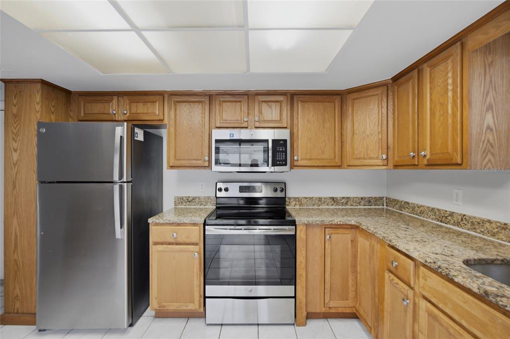A kitchen with oak cabinets, granite countertops, and stainless steel appliances under a drop ceiling — 8207 DEDHAM DRIVE, PORT RICHEY, FL