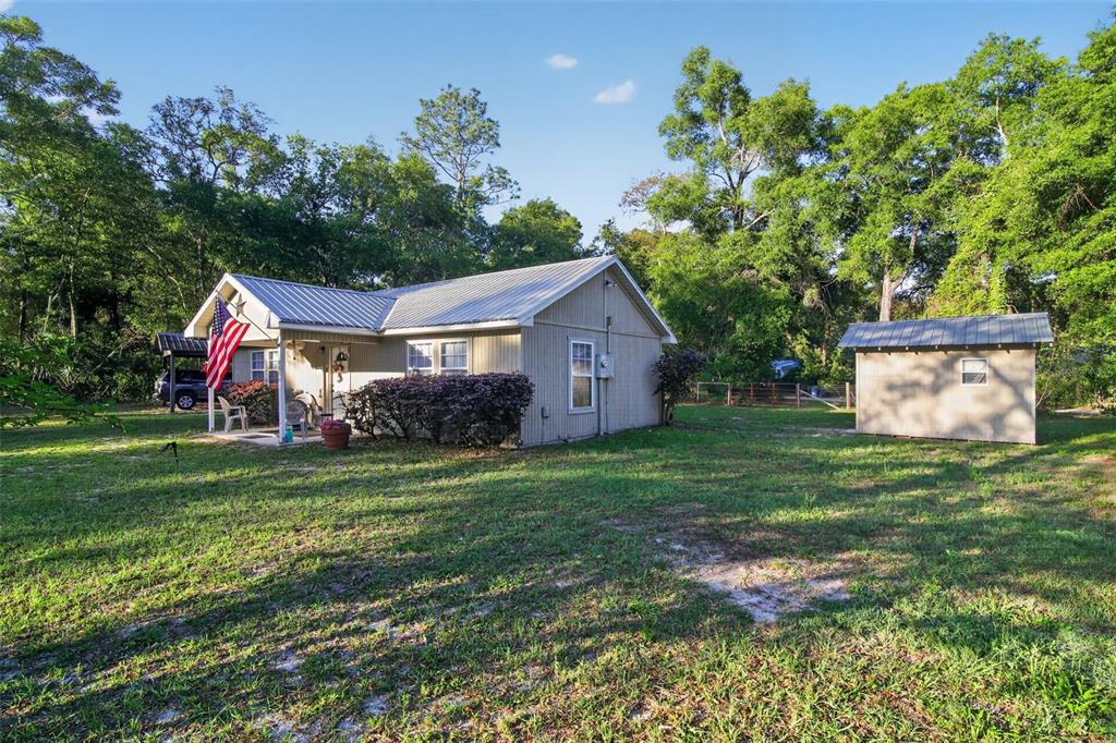 A single-story house with a metal roof and an adjacent shed in a wooded yard — 7390 NW 142ND STREET, TRENTON, FL