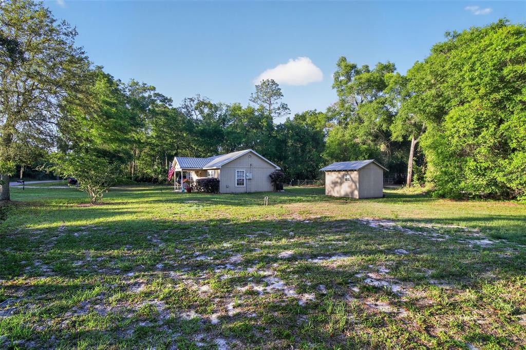 A single-story house and a small detached shed sit on a large, grassy, wooded lot — 7390 NW 142ND STREET, TRENTON, FL