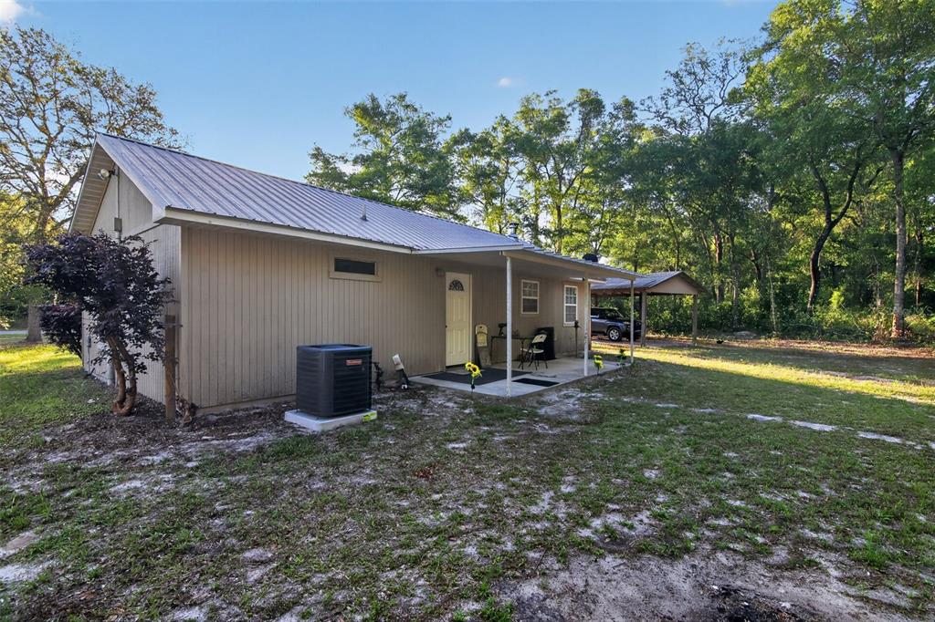A tan house with a metal roof and a covered porch sits on a grassy lot — 7390 NW 142ND STREET, TRENTON, FL