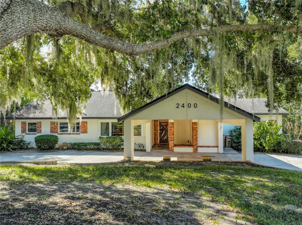 A single-story house with a large covered porch and brick accents under oak trees — 2400 TOPPING PLACE, EUSTIS, FL