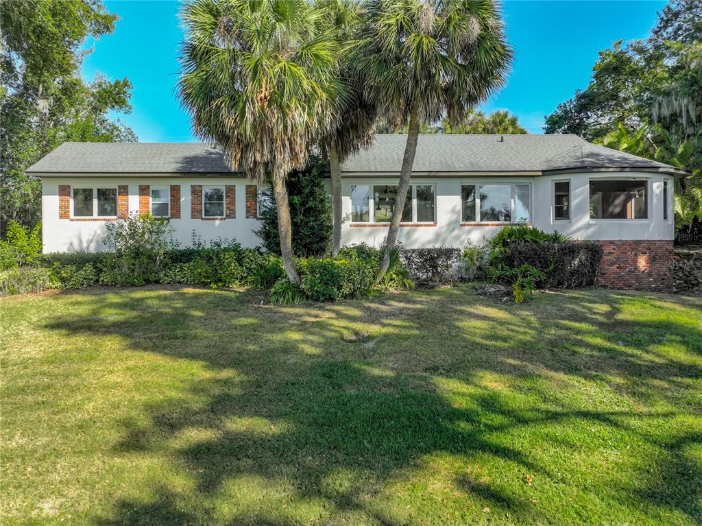 A single-story house with white stucco walls, brick accents, and palm trees in the yard — 2400 TOPPING PLACE, EUSTIS, FL