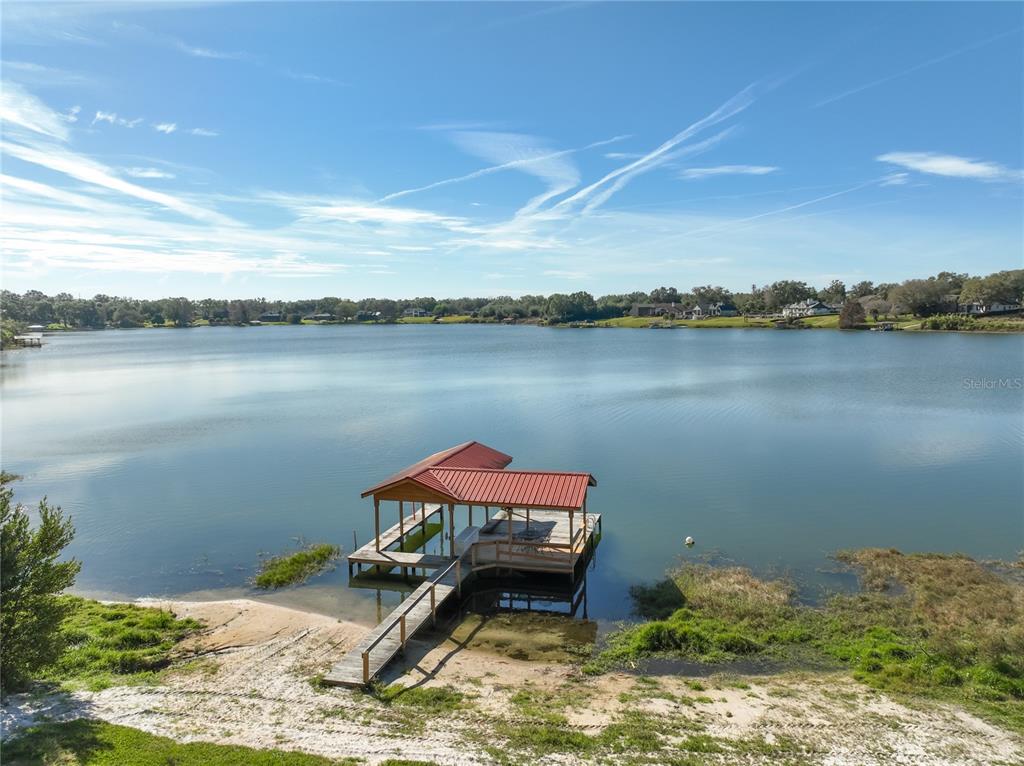A wooden boat dock with a red metal roof extends into a calm lake — 2400 TOPPING PLACE, EUSTIS, FL