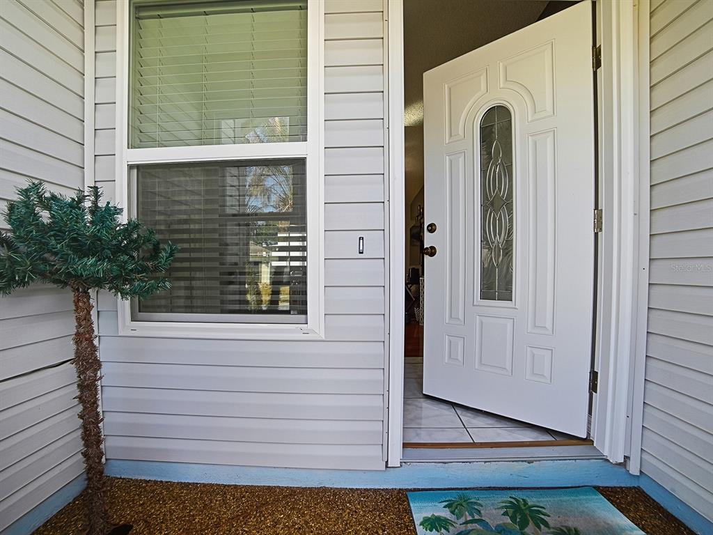 A white front door stands open next to a window on a light-sided house exterior — 32747 WESTWOOD LOOP, LEESBURG, FL
