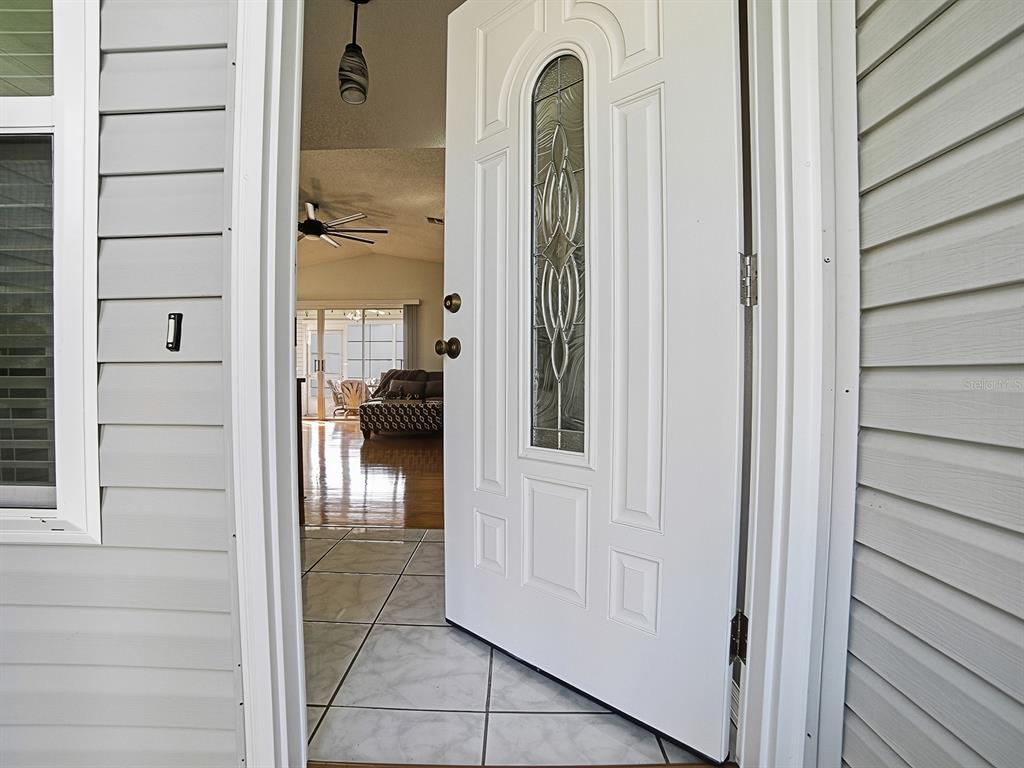 An open white front door reveals a tiled entryway leading into a living room — 32747 WESTWOOD LOOP, LEESBURG, FL