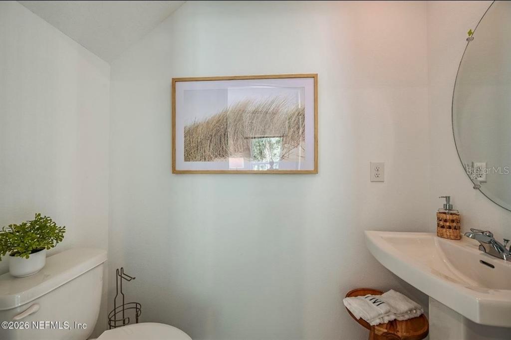 A small bathroom features a pedestal sink, a toilet, a round mirror, and wall art — 7268 SABAL TERRACE, JACKSONVILLE, FL