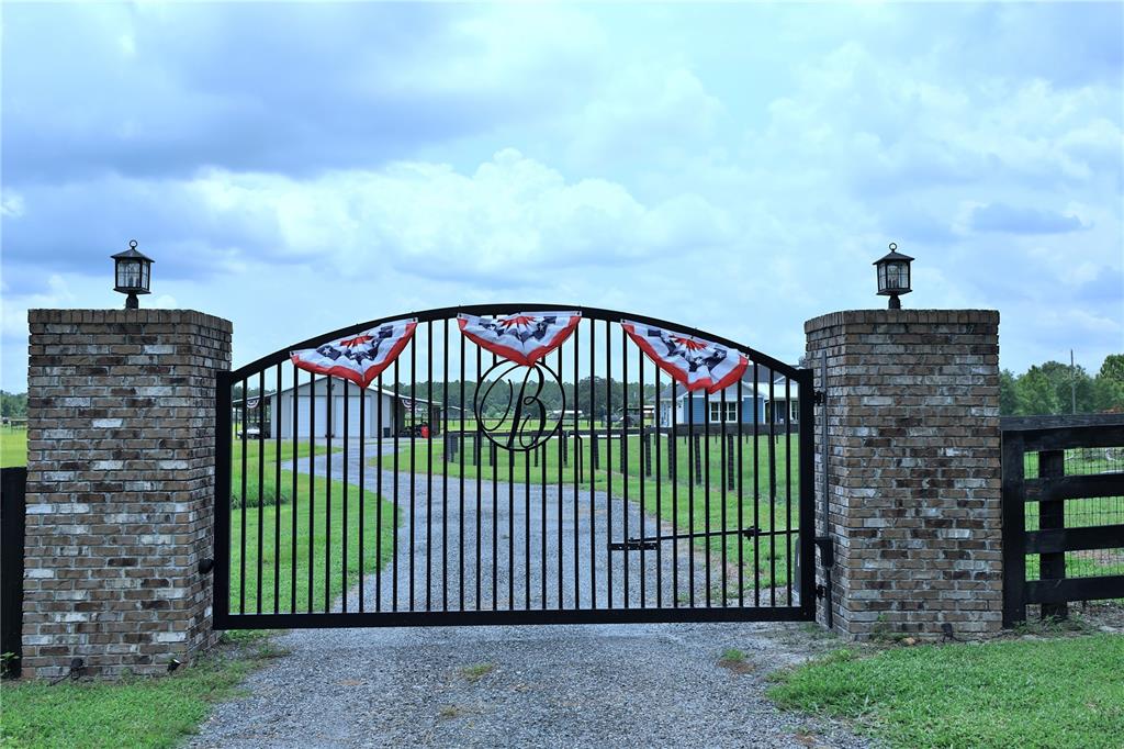 A black metal gate with a central monogram sits between two brick pillars — 10140 CR 209, OXFORD, FL