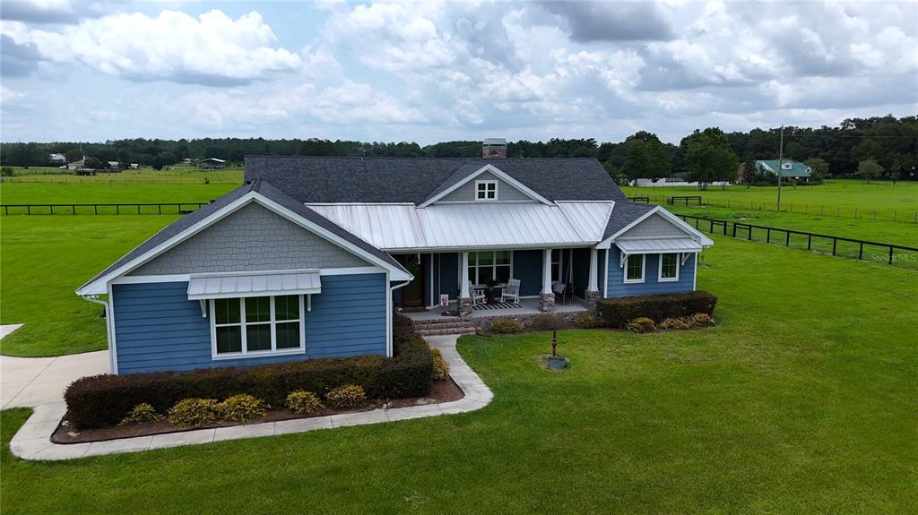 An aerial view of a blue farmhouse with a metal roof and a front porch — 10140 CR 209, OXFORD, FL