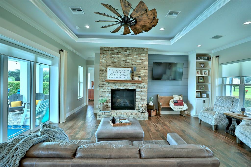A living room features a brick fireplace, wood flooring, a windmill ceiling fan, and built-in shelving — 10140 CR 209, OXFORD, FL