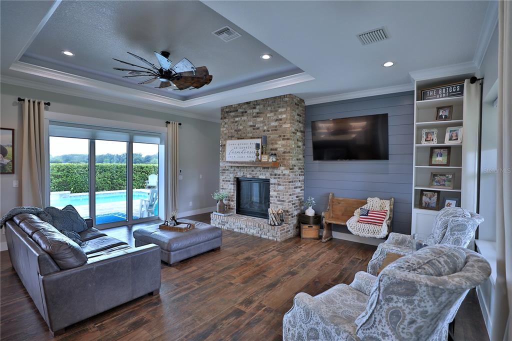 A living room features a brick fireplace, shiplap wall, wood floors, and sliding glass doors — 10140 CR 209, OXFORD, FL