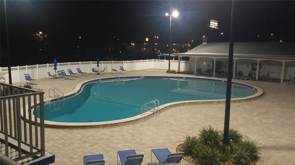 An outdoor swimming pool with lounge chairs at night under bright lighting — 192 NEW ENGLAND AVENUE UNIT 23, PALM HARBOR, FL