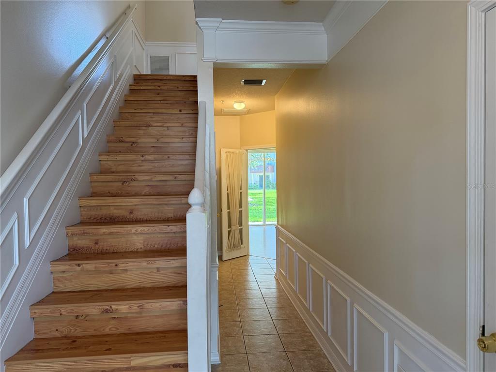 A wooden staircase with white wainscoting stands beside a tiled hallway leading to a doorway — 3146 BAYSHORE OAKS DRIVE, TAMPA, FL