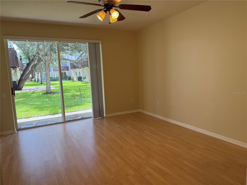 An empty room with light wood-look flooring, beige walls, a ceiling fan, and sliding glass doors — 3146 BAYSHORE OAKS DRIVE, TAMPA, FL