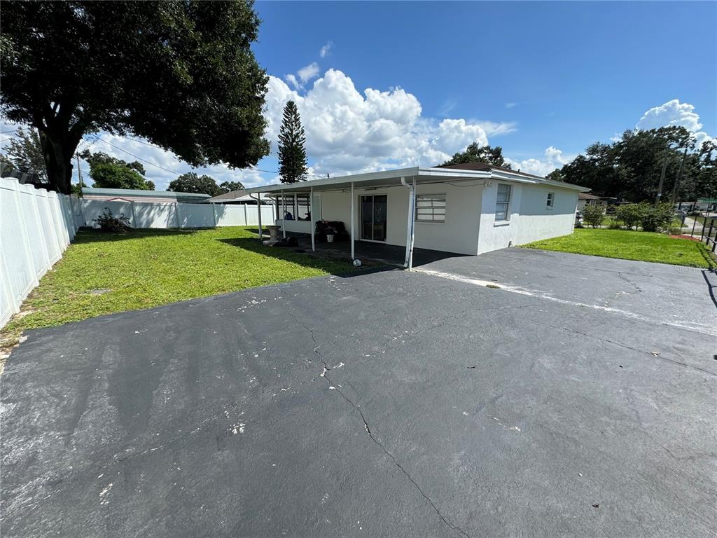 A white house with a covered patio and a large asphalt driveway in the backyard — 7102 REINDEER ROAD, TAMPA, FL