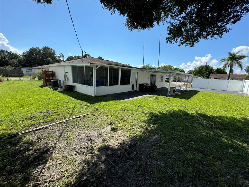 The exterior of a house features a screened-in porch, a covered patio, and a grassy yard — 7102 REINDEER ROAD, TAMPA, FL