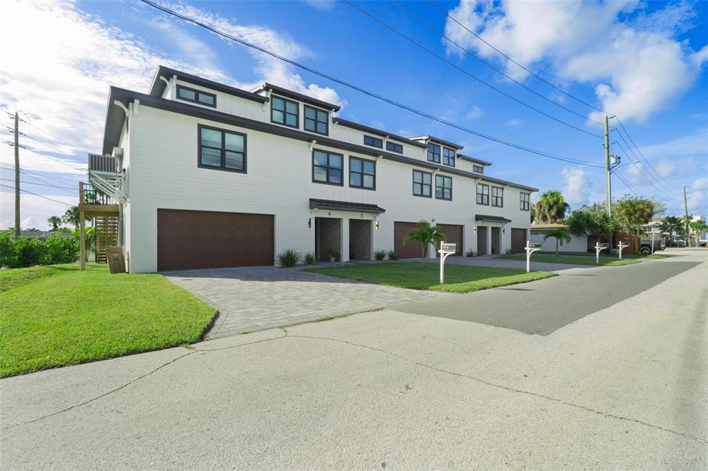 A multi-unit residential building with white siding, dark garage doors, and a paved driveway — 187 145TH AVENUE E UNIT 3, MADEIRA BEACH, FL