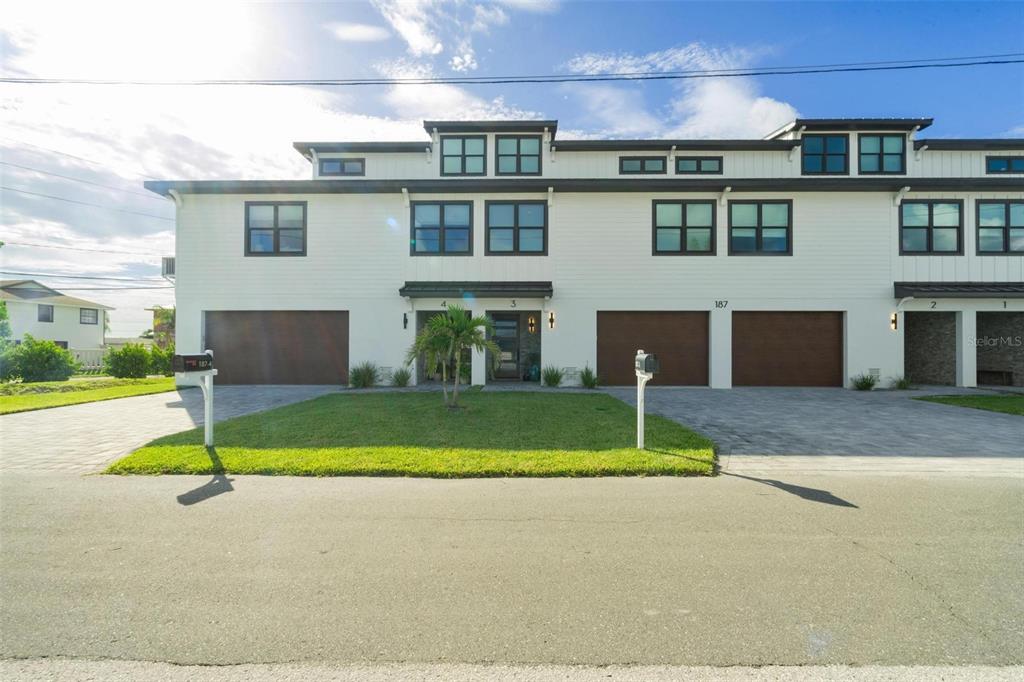 A multi-unit residential building with white siding, dark-framed windows, and attached garages — 187 145TH AVENUE E UNIT 3, MADEIRA BEACH, FL