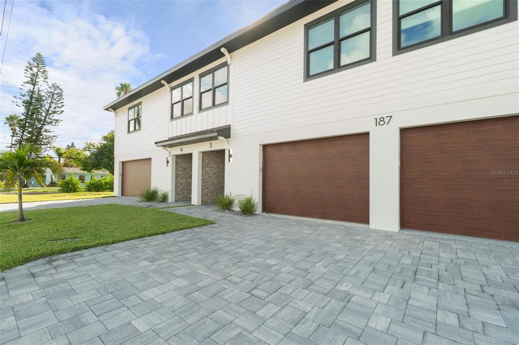 A modern two-story townhouse exterior features white siding, dark-framed windows, and multiple garage doors — 187 145TH AVENUE E UNIT 3, MADEIRA BEACH, FL