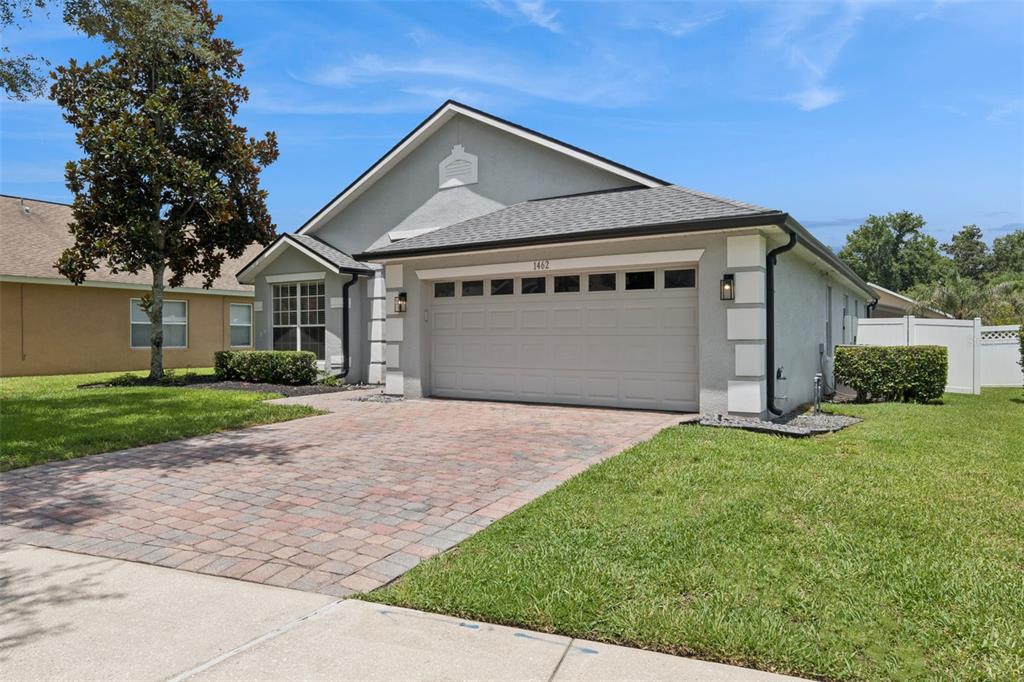 A single-story house with a gray stucco exterior, a brick paver driveway, and a garage — 1462 BARN OWL LOOP, SANFORD, FL
