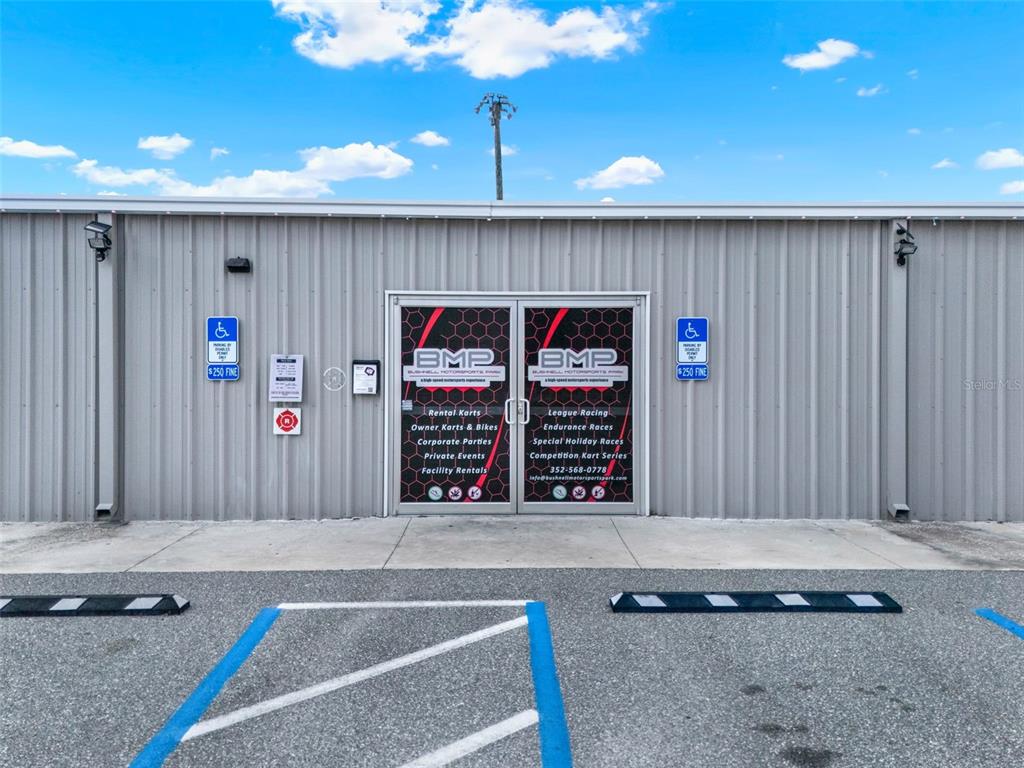 The exterior of a metal building features double glass doors with signage for a motorsports park — 5765 PIT ROAD, BUSHNELL, FL