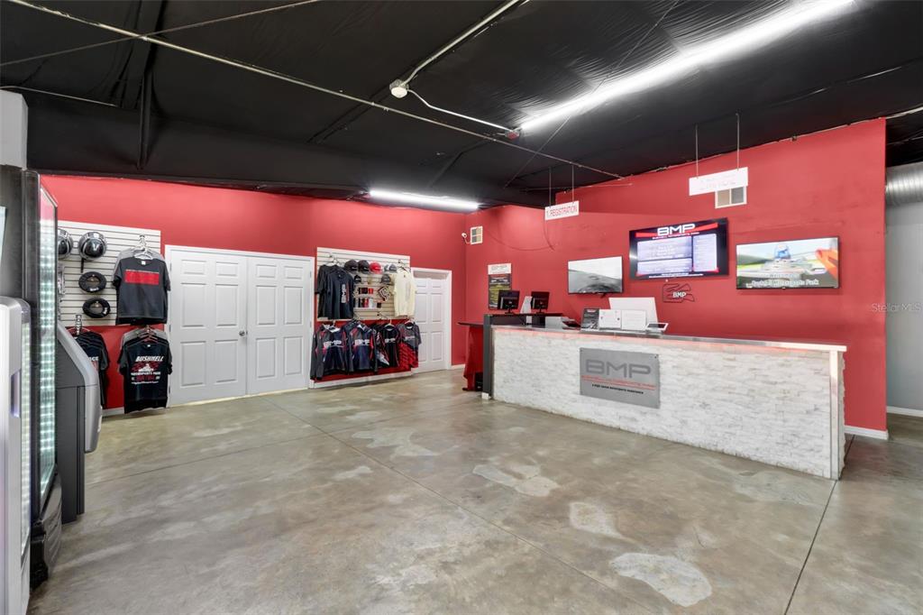 A commercial reception area features a stone-front desk, red walls, and branded apparel displays — 5765 PIT ROAD, BUSHNELL, FL