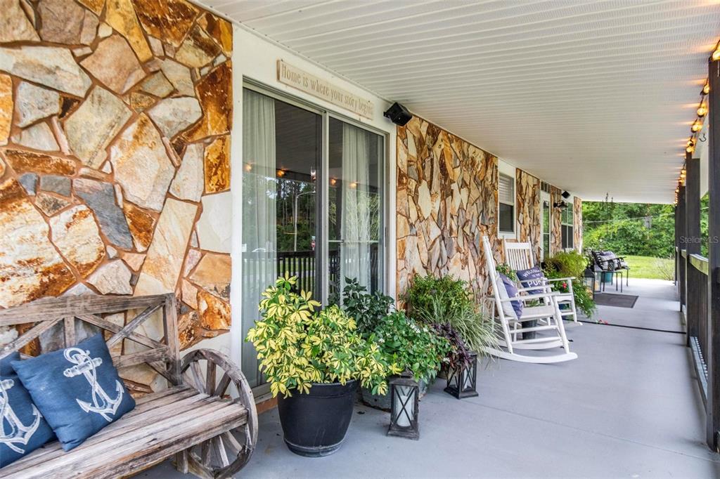 A covered porch features a stone wall, a wooden wagon-wheel bench, and white rocking chairs — 702 N CHAPEL STREET, BUNNELL, FL