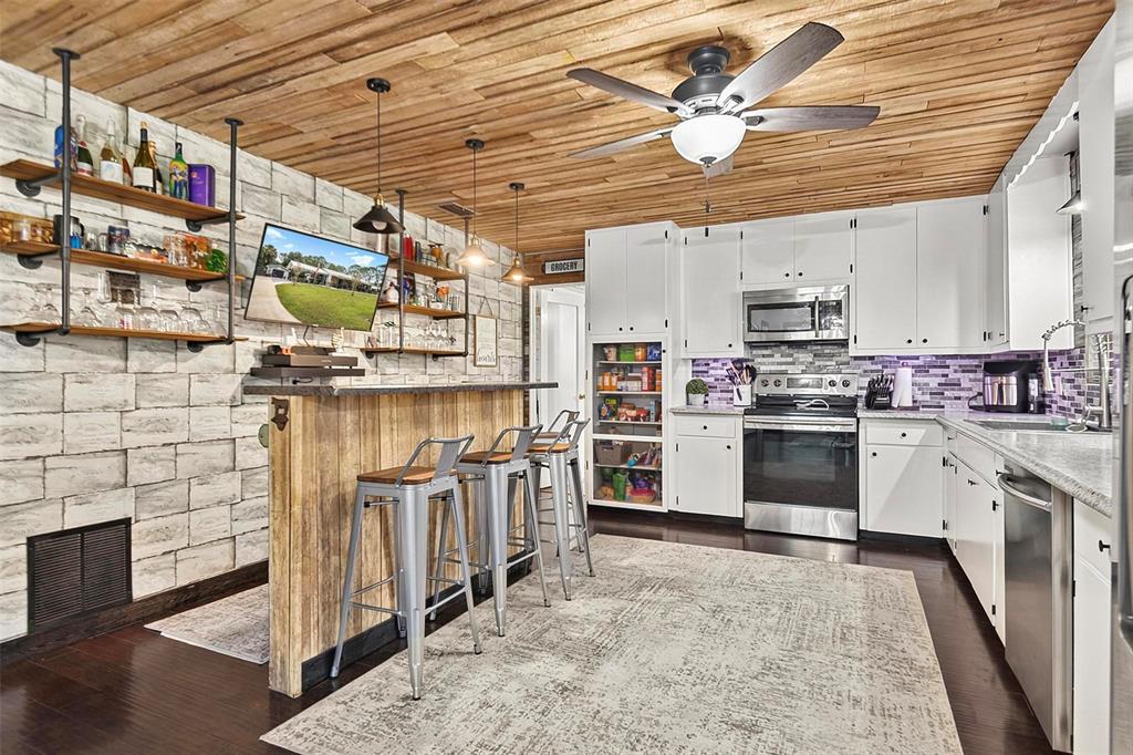 A kitchen with a wooden ceiling, stone-look wall, bar seating, and white cabinetry — 702 N CHAPEL STREET, BUNNELL, FL