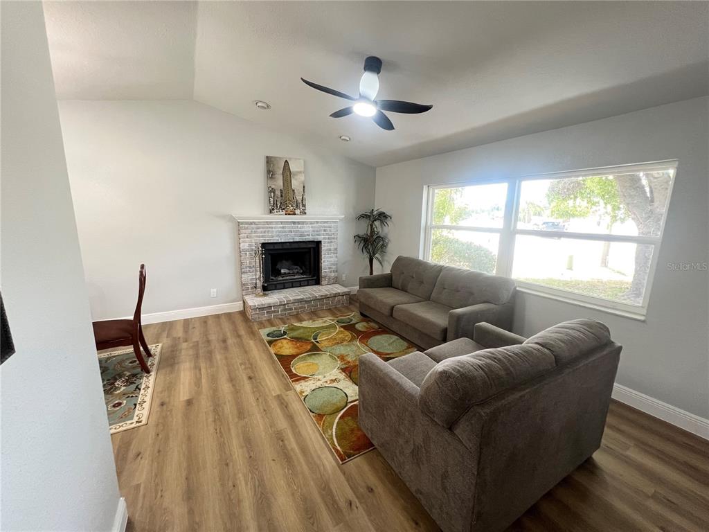 A living room features a brick fireplace, gray sofas, a patterned rug, and wood flooring — 12195 71ST WAY, LARGO, FL