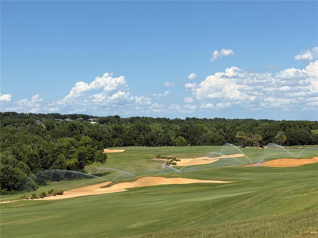 A wide view of a golf course fairway with sand bunkers and active irrigation sprinklers — 15831 VETTA DRIVE, MONTVERDE, FL