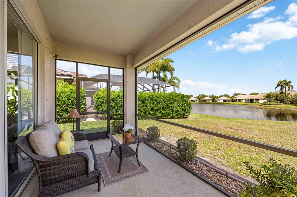 A screened-in patio features wicker furniture overlooking a grassy lawn and a small lake — 8769 MONTEREY BAY LOOP, BRADENTON, FL