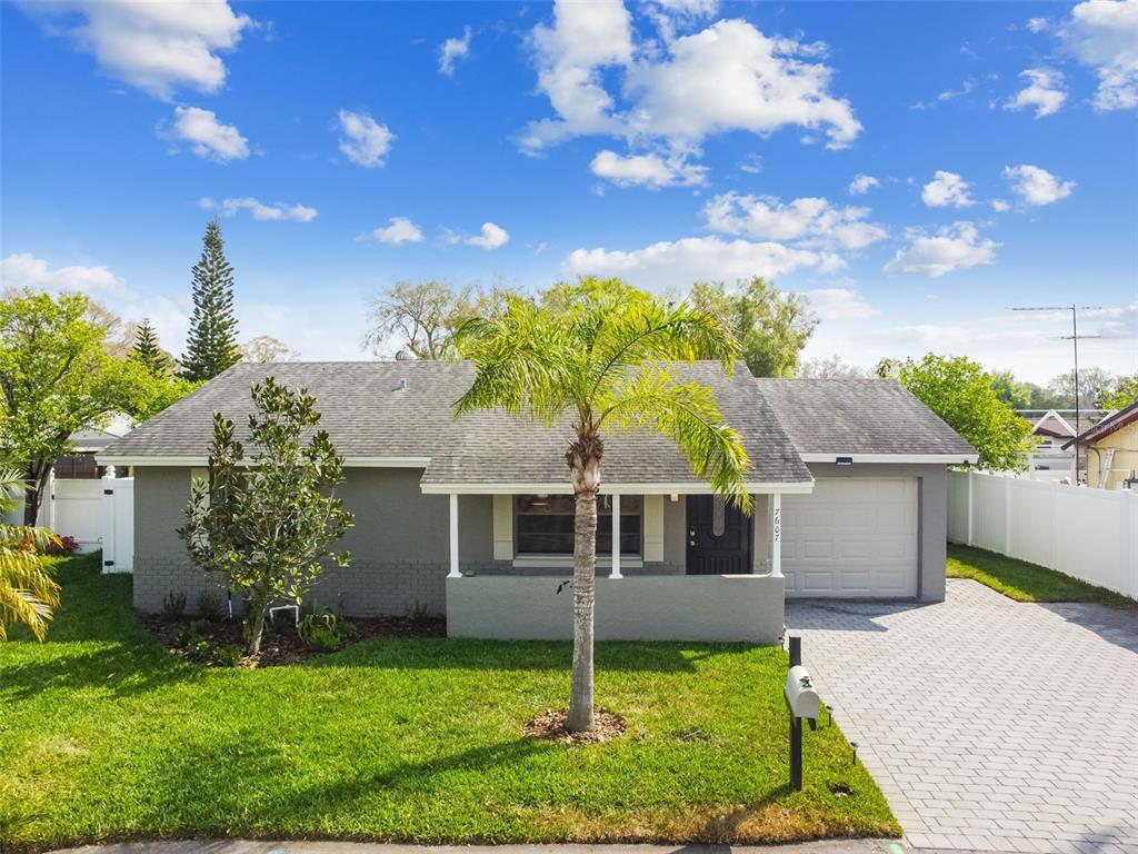 A single-story gray house features a front porch, a palm tree, and a paved driveway — 7607 WOODLAND OAKS COURT, TAMPA, FL