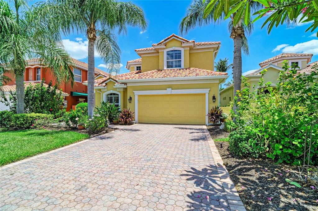 A yellow two-story house with a tiled roof and a paved driveway under a blue sky — 308 10TH AVENUE E, PALMETTO, FL