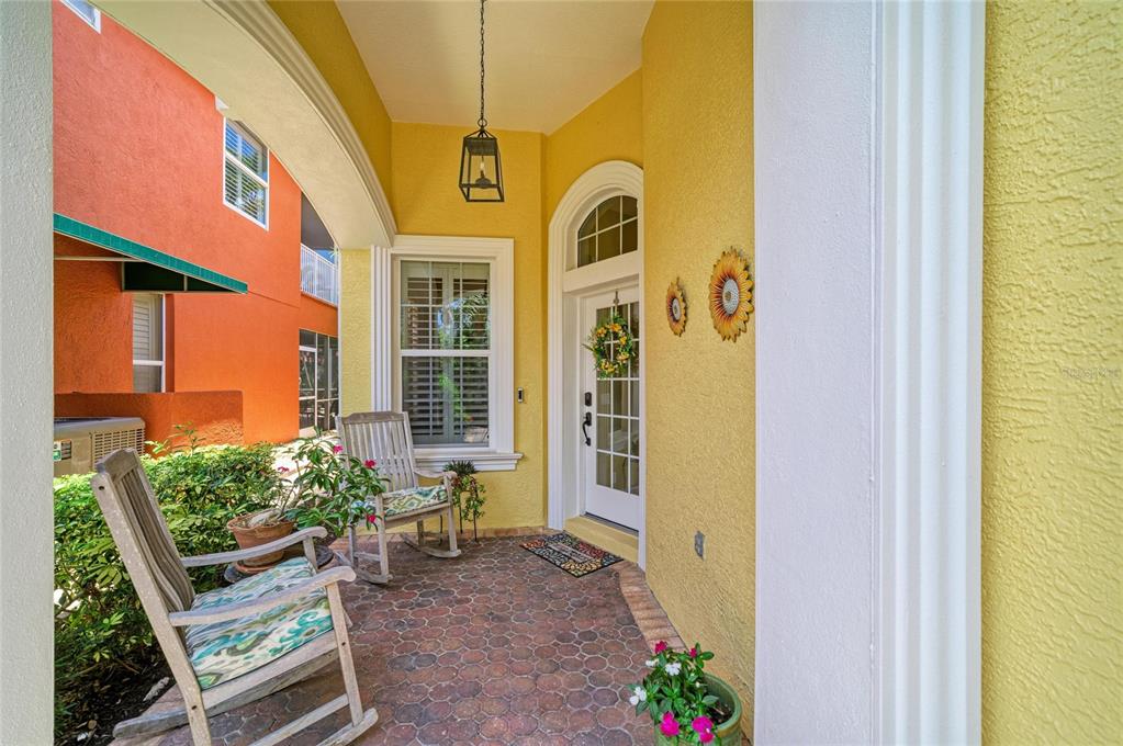 A covered porch features a brick floor, two rocking chairs, and a yellow exterior wall — 308 10TH AVENUE E, PALMETTO, FL