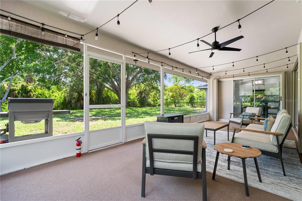 A screened-in patio features outdoor furniture, a ceiling fan, string lights, and a backyard view — 313 GOLD TREE, PUNTA GORDA, FL