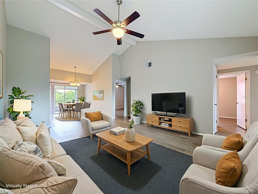 This living room features vaulted ceilings, a ceiling fan, and light wood-look flooring — 7606 WOODLAND OAKS COURT, TAMPA, FL