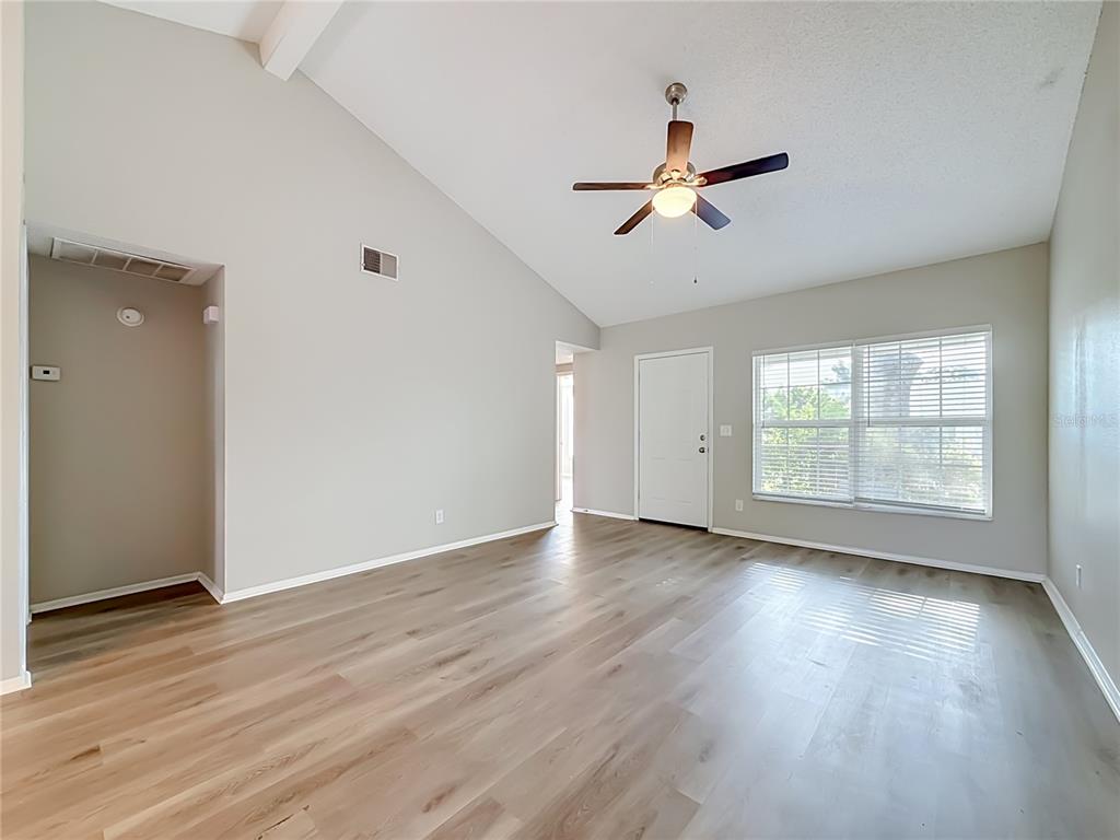 An empty living room features light wood-look flooring, vaulted ceilings, and a ceiling fan — 7606 WOODLAND OAKS COURT, TAMPA, FL