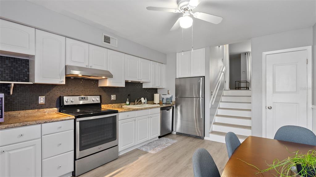 A kitchen features white cabinets, stainless steel appliances, a black tile backsplash, and a dining area — 4227 LA PALMA COURT, TAMPA, FL