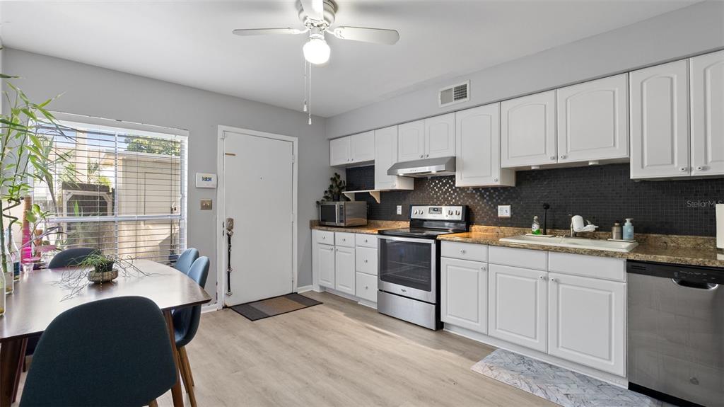 A kitchen with white cabinets, stainless steel appliances, and a dark tiled backsplash — 4227 LA PALMA COURT, TAMPA, FL