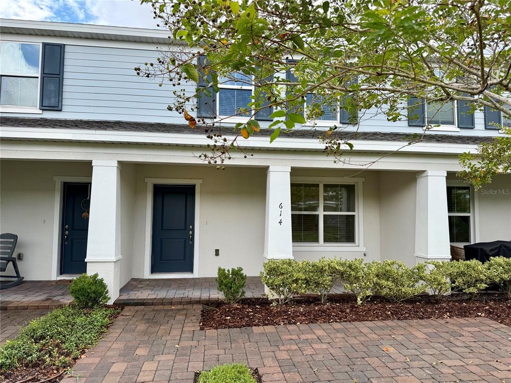 The exterior of a two-story townhouse features a covered porch, dark blue doors, and pavers — 614 CHEVAL LANE, DEBARY, FL