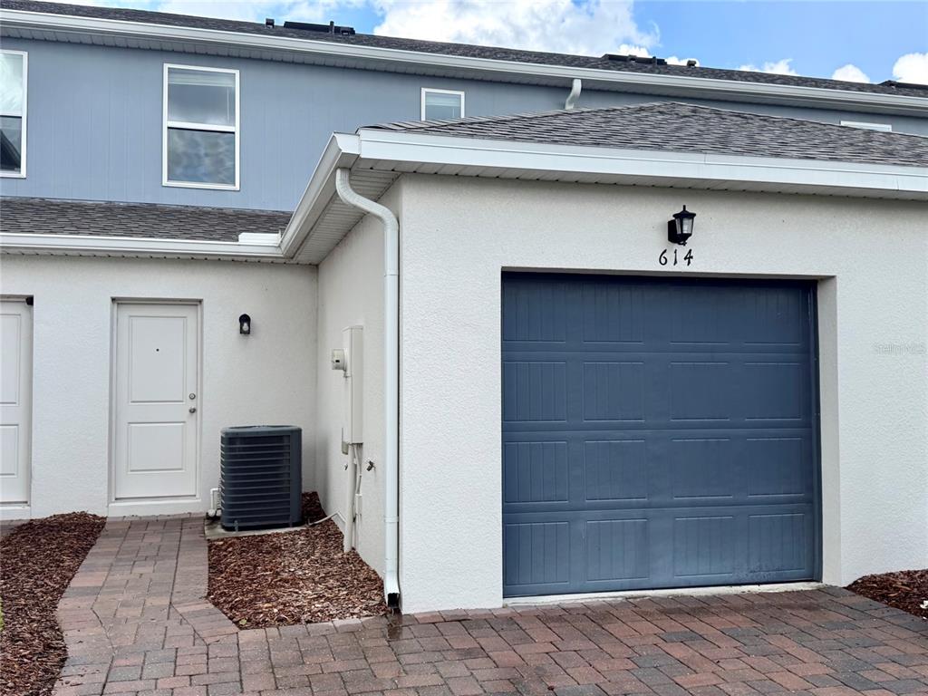 A white stucco townhouse exterior features a blue garage door, a front door, and an AC unit — 614 CHEVAL LANE, DEBARY, FL