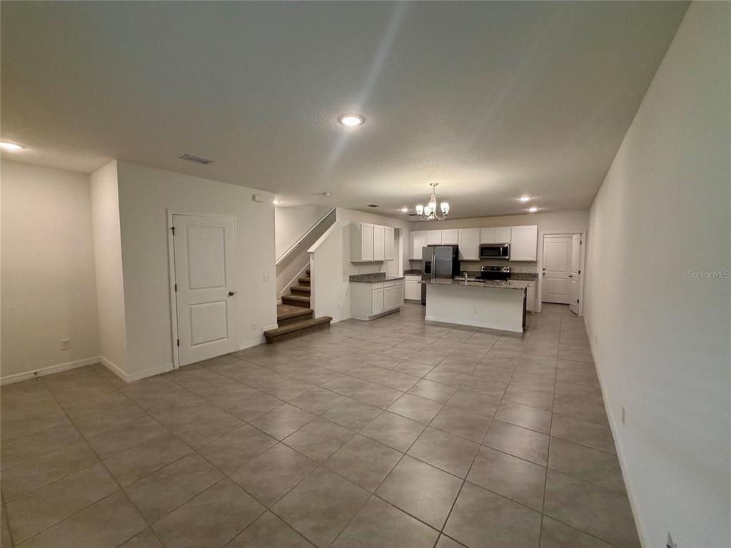 An open-concept kitchen and living area features tile flooring, white cabinetry, and a staircase — 614 CHEVAL LANE, DEBARY, FL