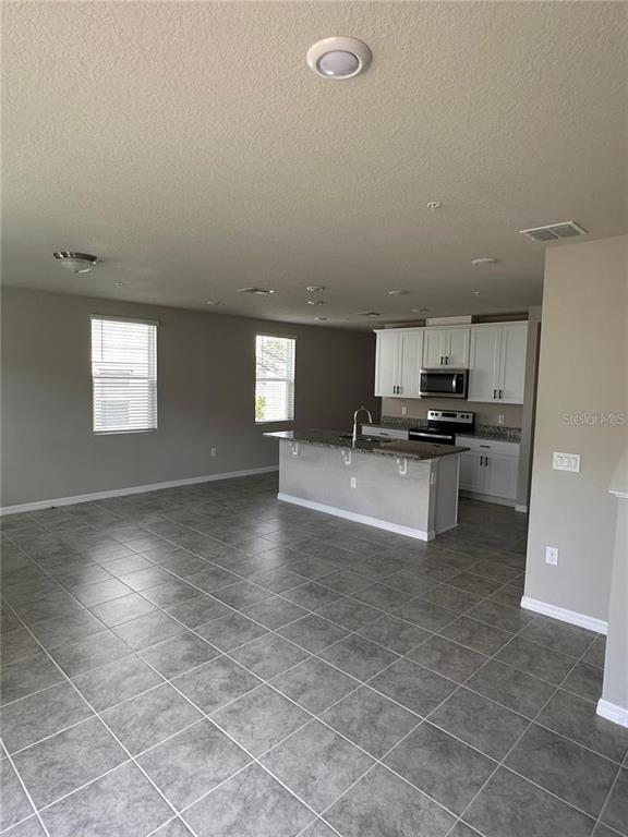 A kitchen with white cabinets and a center island opens into a tiled living area — 2040 MILKWEED STREET, OCOEE, FL